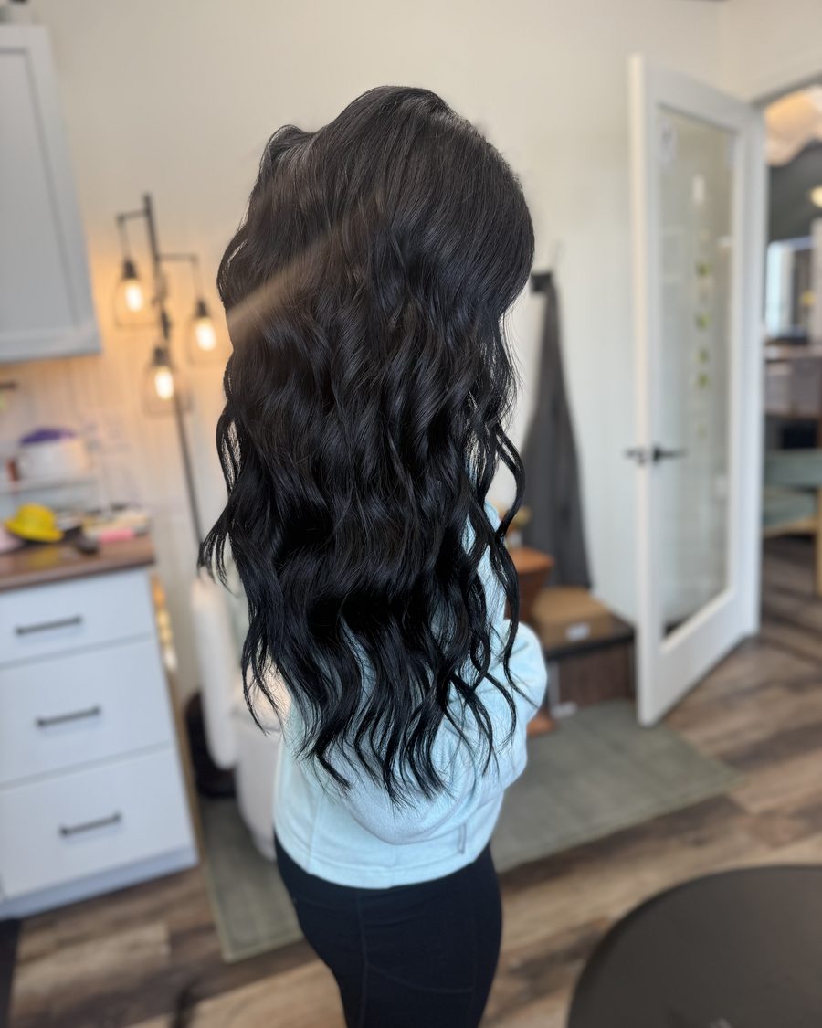 After: the same guest with long, full black waves following a hand-tied Invisible Bead Extensions install at Emerald Salon & Suites, Hiawatha, Iowa