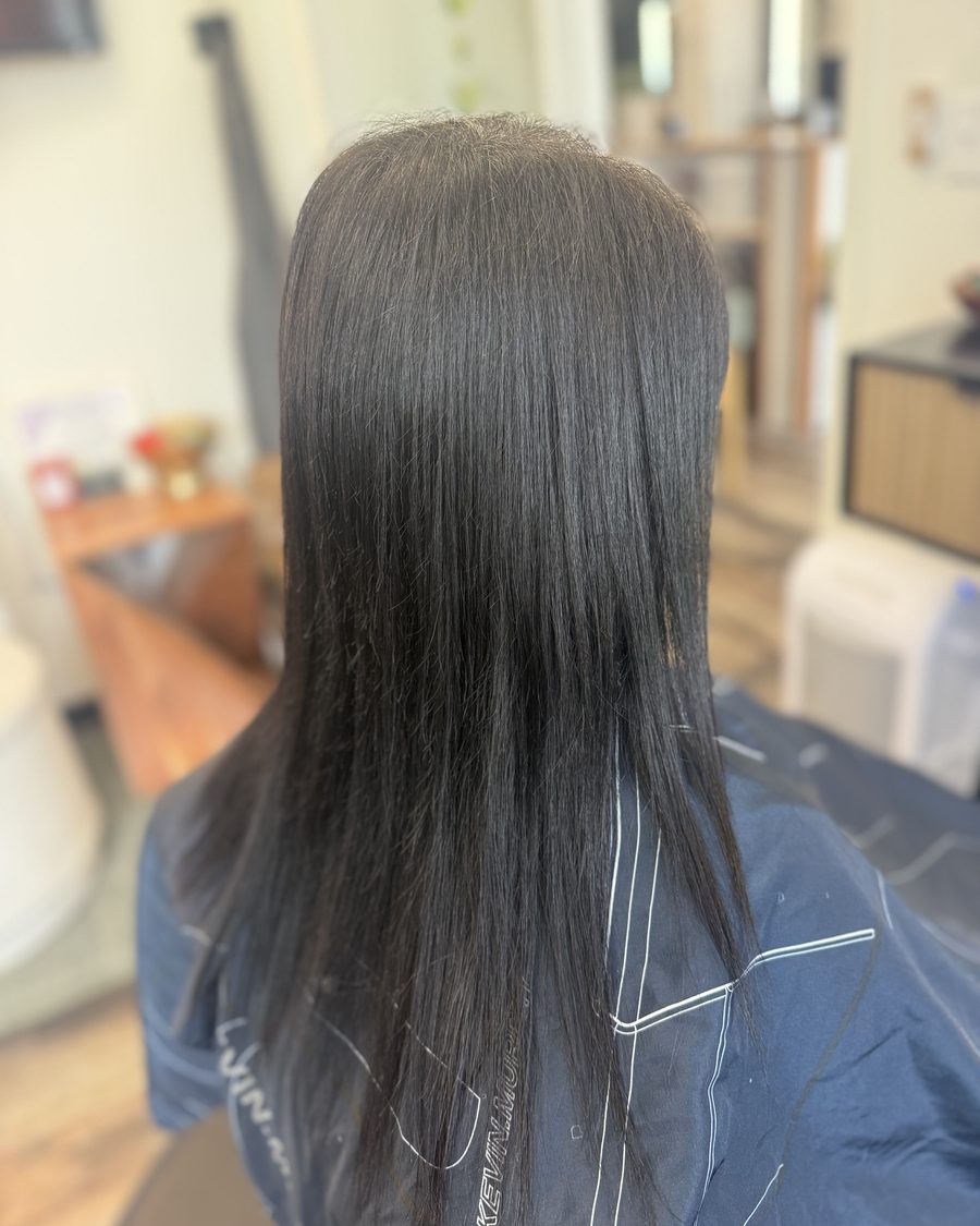 Before: fine, straight, dark hair with thin ends, photographed from behind in the salon chair before Invisible Bead Extensions