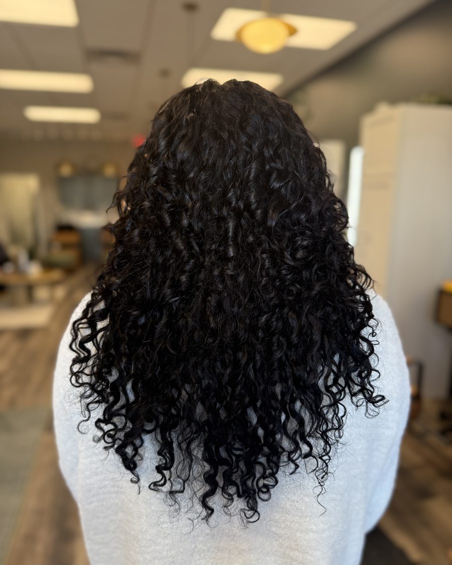 Long, defined black curls after Invisible Bead Extensions on naturally curly hair at Emerald Salon & Suites near Cedar Rapids, Iowa
